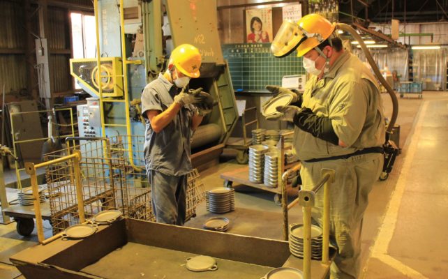 Two Oigen foundry workers inspecting cast-iron for imperfections.